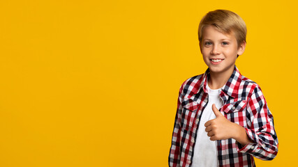 Cheerful confident european teen boy showing thumb up looking at camera, on yellow background