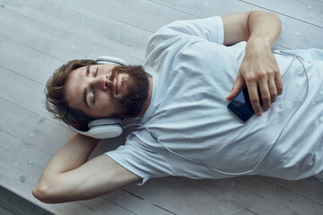 man in white t-shirt lying on the windowsill wearing headphones hipster