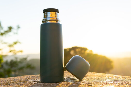Thermos with cup on stone surface in sunlight