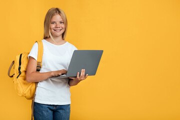 Happy pretty adolescent european blonde girl with backpack studying with laptop