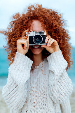 Smiling red haired female taking picture on vintage photo camera