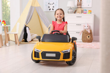 Adorable child driving toy car in room at home