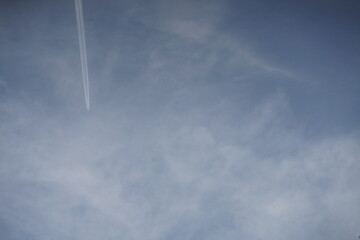 Blauer Himmel mit weißen Wolken und Flugzeug mit Kondensstreifen in geradem Flug auf und davon