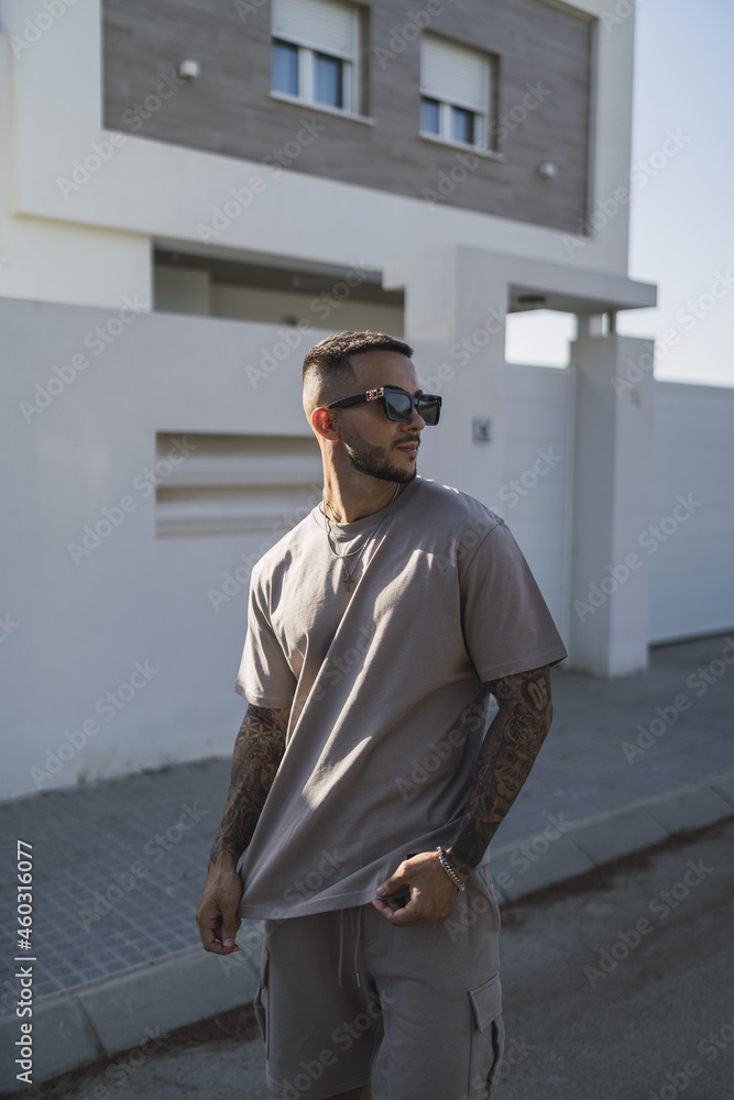 Wall mural vertical shot of a young handsome caucasian male with glasses standing outdoors