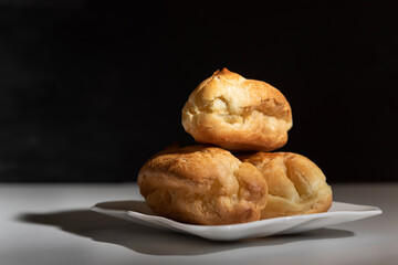 Delicious profiteroles or eclairs without cream on saucer. Black background.
