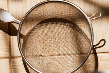 Metal mesh sieve on the tiles on the floor illuminated by side light. Selective focus.