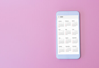 White smart phone show calendar App 2022 on pink background. New Year Concept.