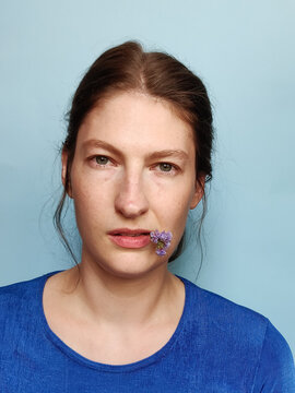 Portrait Of A Woman On A Blue Background Holding A Flower In Lips