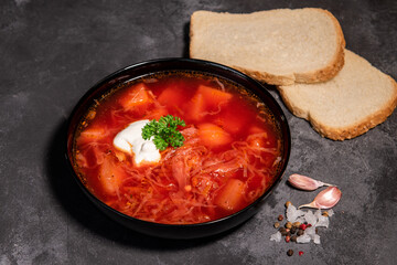 Borsch. Ukrainian soup. Red soup. Borsch with sour cream and onions, white bread. Traditional Russian borsch with sour cream. The concept of delicious food with sour cream on a black background