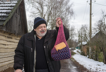 Portrait of smiling elderly peasant walking with string bag  to local bath-house on an empty street...