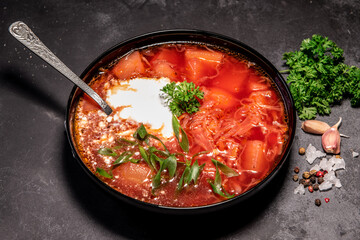 Borsch. Ukrainian soup. Red soup. Borsch with sour cream and onions, white bread. Traditional Russian borsch with sour cream. The concept of delicious food with sour cream on a black background
