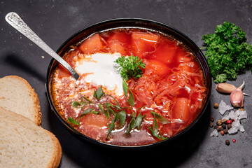 Borsch. Ukrainian soup. Red soup. Borsch with sour cream and onions, white bread. Traditional Russian borsch with sour cream. The concept of delicious food with sour cream on a black background