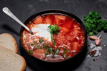 Borsch. Ukrainian soup. Red soup. Borsch with sour cream and onions, white bread. Traditional Russian borsch with sour cream. The concept of delicious food with sour cream on a black background