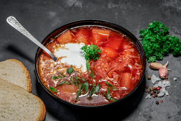 Borsch. Ukrainian soup. Red soup. Borsch with sour cream and onions, white bread. Traditional Russian borsch with sour cream. The concept of delicious food with sour cream on a black background