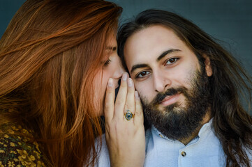 Portrait of a young couple where a red-haired woman tells a secret to the man bearded her ear...