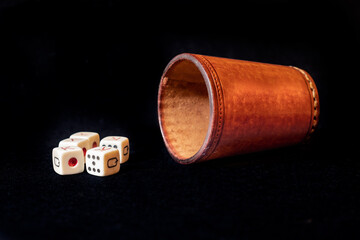 Leather dice cup with five poker dice on a black mat