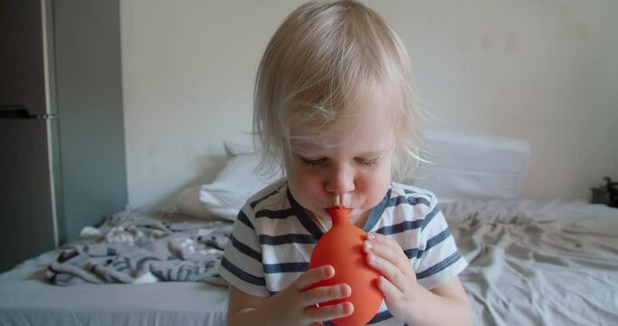 Carefree childhood of cute baby children blowing orange balloon playing and smiling indoors. 2 years old blonde hair girl with strong lungs