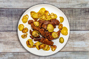 Grilled beef liver with jiló on white plate top view. Typical Brazilian dish from the state of Minas Gerais