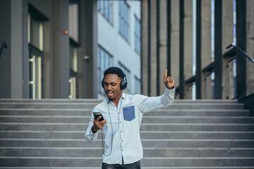 young african student listening to music from smartphone using big headphones, smiling from the convenience of using the app