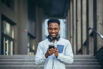 Young african american man happy with win looks at phone rejoices and smiles in casual clothes
