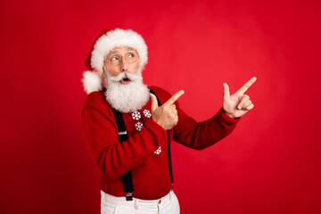 Fototapeta na wymiar Photo of aged man wear santa hat amazed point fingers empty space ad promo direct select isolated over red color background
