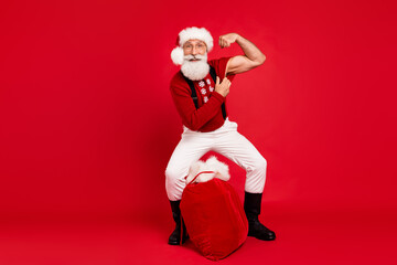 Full size photo of santa happy positive smile show hand muscles biceps strong sack gift isolated over red color background