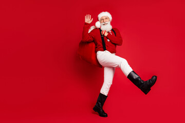 Full length body size view of nice cheerful Santa carrying giftboxes waving hi hello isolated over bright red color background