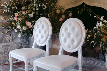 Classic white chairs with floral arrangements in the background.