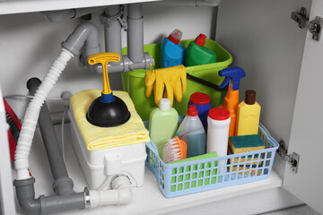 Open under sink cabinet with different cleaning supplies in kitchen