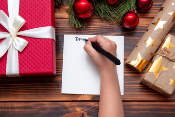 Cropped shot of a child writing a letter to Santa Claus with a black marker on a wooden table with...