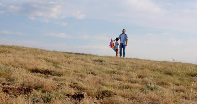 A boy and his father prepare to launch a kite on a yellow field against blue sky. Father and son play together, strong friendship father and son. 4k slow motion