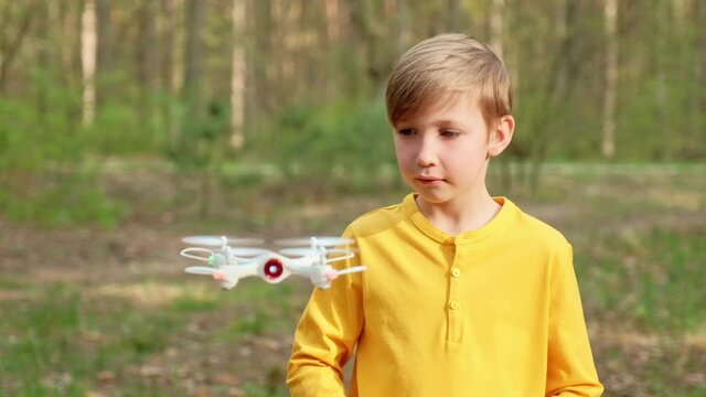 Child launches the drone outdoors. Boy plays with a quadrocopter on the nature. White boy is learning  to control a drone in the Park.
