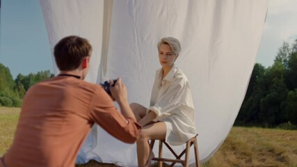 Behind the scenes of professional photoshoot. Male photographer with analog film camera give directions to young female model on beautiful outdoors photo set. Cinematic photography inspiration