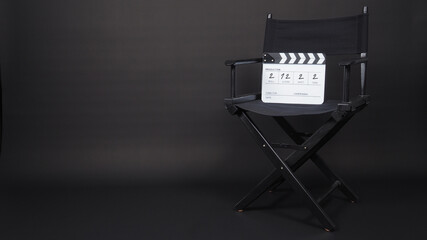 Black Director chair and white clapper board or movie slate  on black background. It has written in...