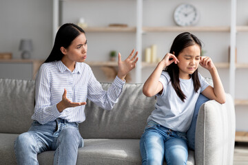 Mother daughter conflict. Young asian mom trying to speak to her offended little child, sitting...