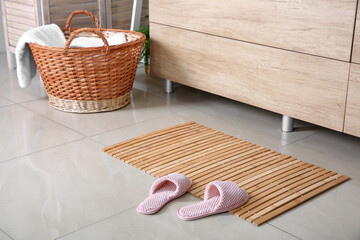 Fototapeta na wymiar Wooden mat with slippers on floor in bathroom