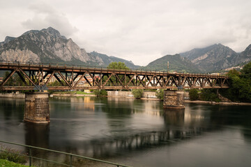Railroad train bridge over Adda River in Lecco city on a cloudy day. - obrazy, fototapety, plakaty