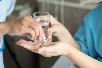 Close up of nurse hand putting white pill into patient hand.Sick female holding glass for taking medicines, antidepressant, painkiller or antibiotic.Pharmacy and healthcare concept