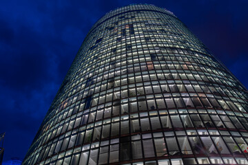 Rising skyward from street below high-rise commercial office building at night with light in all windows.