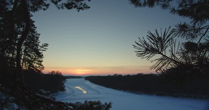 Beautiful winter snowy landscape while sunset. Beautiful view of a wide frozen river with snow-covered branches of trees. Desna river under ice and snow in Ukraine.