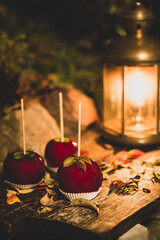 Trio of glistening caramelized apples, poised on rustic wood, illuminated by the warm embrace of a lantern's flame.
