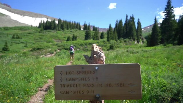 Hiking Sign on Conundrum Hot Spring Trail and Woman With Backpack in Green Landscape of Rocky Mountains, Colorado USA, Full Frame