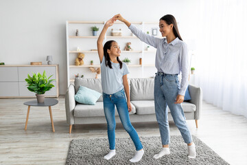 Cheerful asian mother and daughter dancing to music, holding hands and enjoying spending time together at home