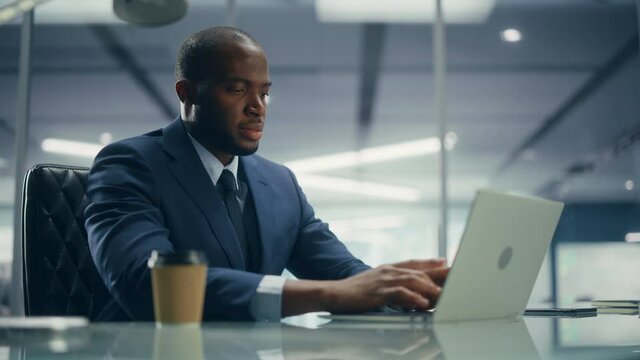 Top Management Modern Office: Successful Black Businessman in Tailored Suit Working on Laptop Computer. Professional African American CEO Managing Stock Markted Investment Clients Accounts