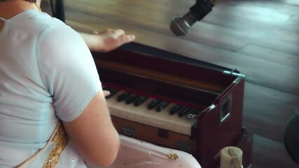 a girl sitting on a wooden floor and playing a keyboard ethnic Indian instrument