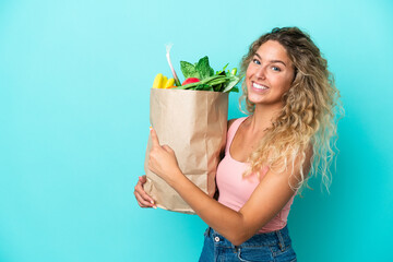 Girl with curly hair holding a grocery shopping bag isolated on green background pointing back
