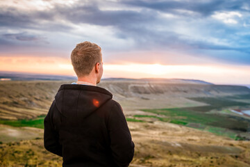 A young man conquered the top of the mountain at dawn. Beautiful mountain landscape with a slope. The concept of enjoying nature.