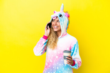 Girl with curly hair wearing a unicorn pajama isolated on yellow background holding coffee to take...