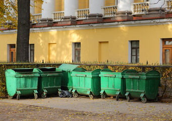 Mobile plastic green garbage containers at the yellow wall of the old building, Admiralteysky Passage, St. Petersburg, Russia, October 2021