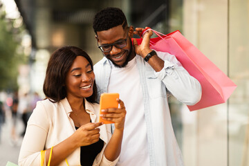 Happy black couple using phone with shopping bags